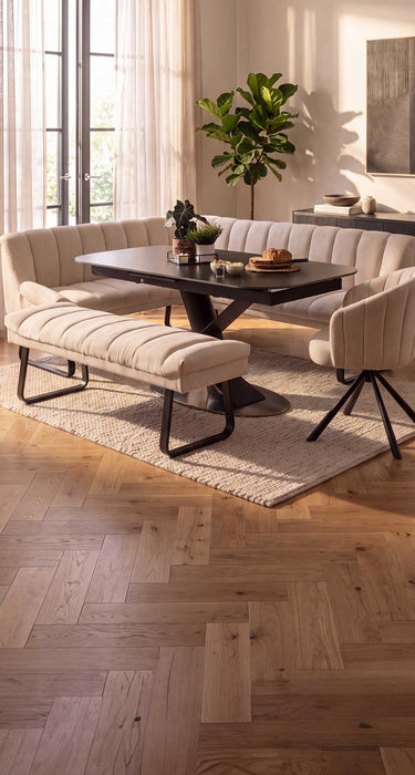 A modern dining room setup featuring a cream tufted corner dining bench, a matching backless bench, a black ceramic marble dining table, and a cream swivel chair on a light rug.