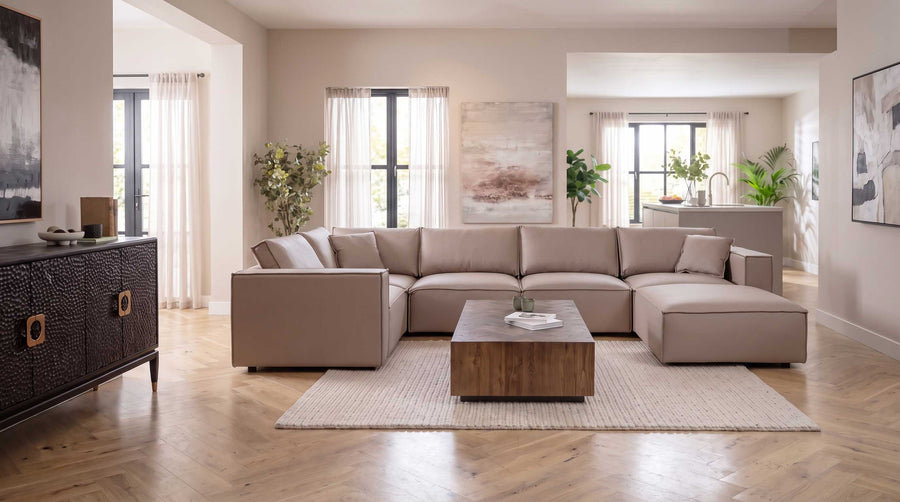 A large modular beige leather corner sofa, styled in a bright, contemporary living room with a wooden coffee table, textured rug, and wood floors.
